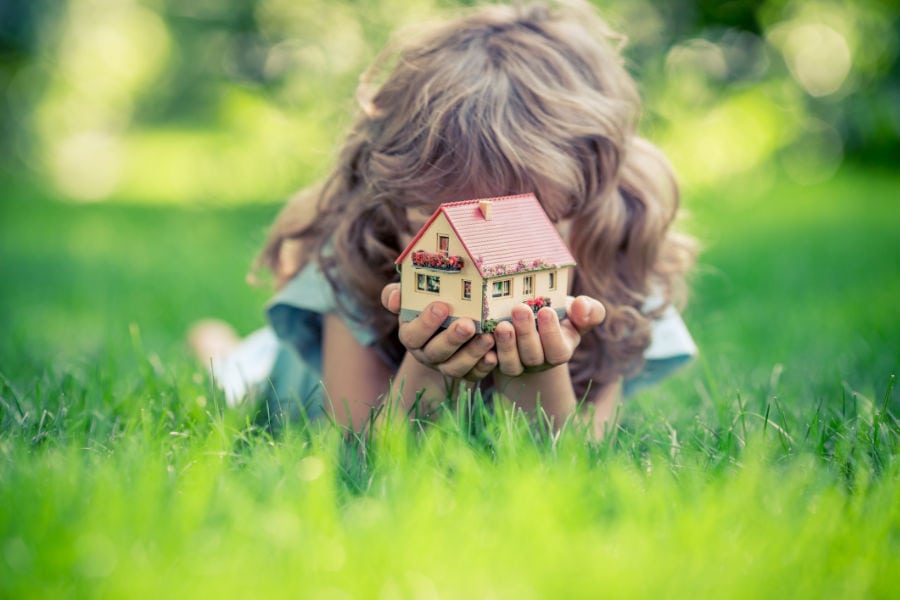 Young girl laying in field, holding a miniature house to represent how an air conditioner works.
