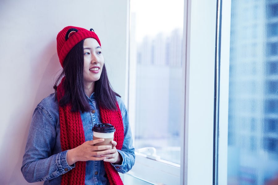 Woman in red hat and scarf by window in winter.