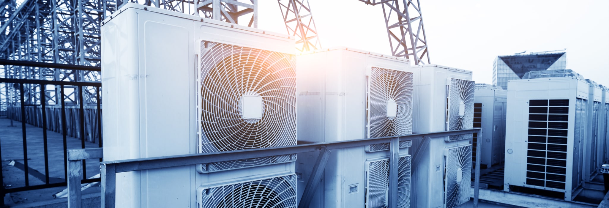 Air conditioner units (HVAC) on a roof of industrial building with blue sky and clouds in the background.