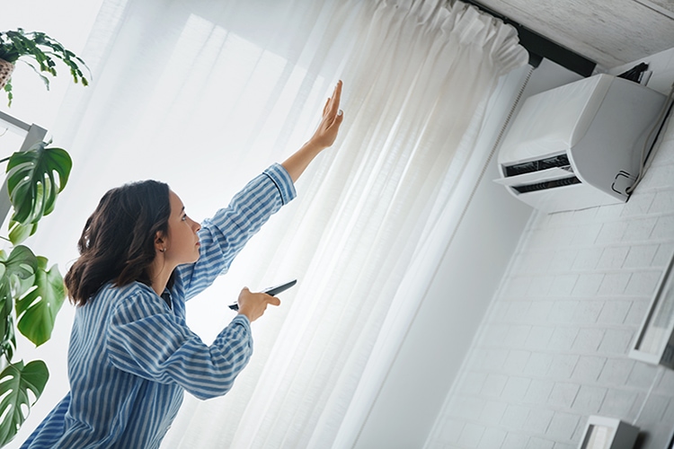 Blog Title: How Does Your Central Air Conditioner Cool Your Home? Photo: Person turning on Air Conditioner