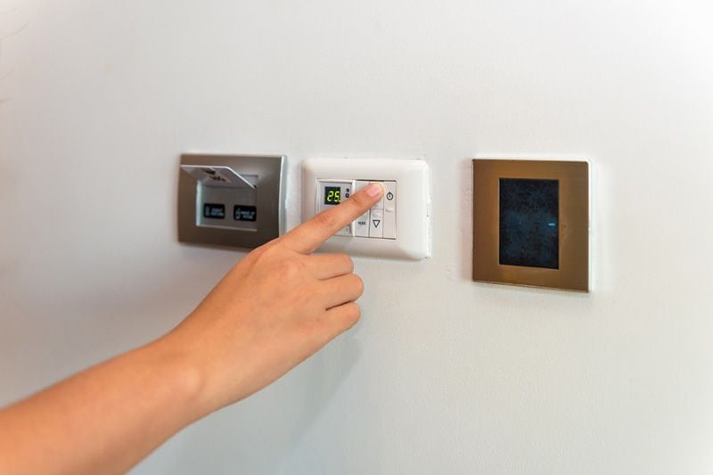 Image of someone pressing on a control panel attached to different HVAC systems. Heat Pump Versus Furnace.