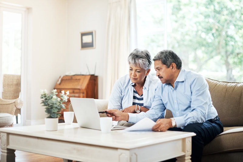 Senior couple sitting on couch with laptop, reviewing what air purifiers and air filters do.