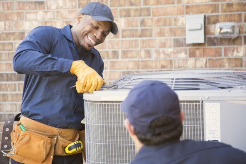 Two HVAC technicians opening an outdoor air conditioning unit.