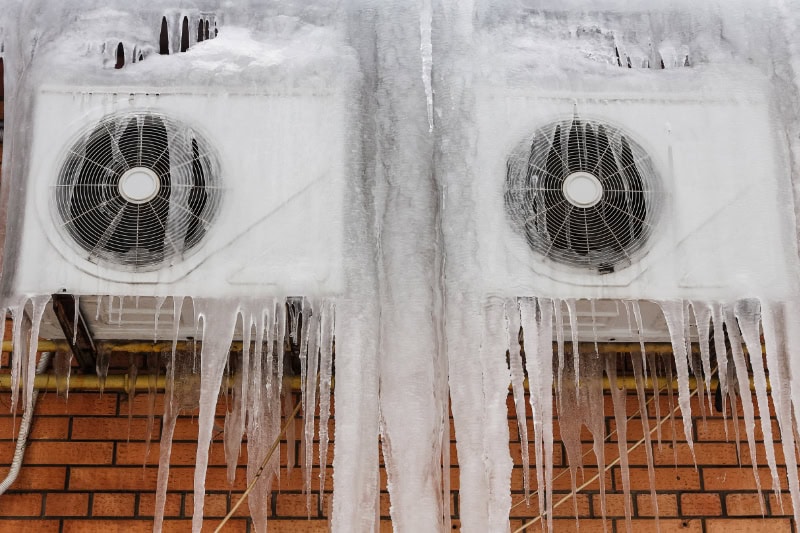 Two outdoor air conditioners mounted to brick wall and covered in ice.