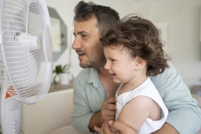 father and child sitting in front of a fan.
