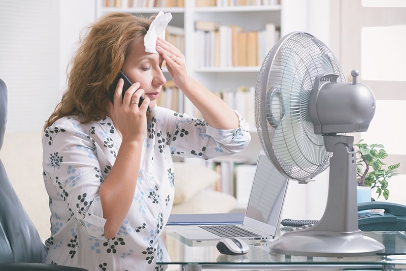 Woman trying to stay cool while working on her laptop due to a broken air conditioner.