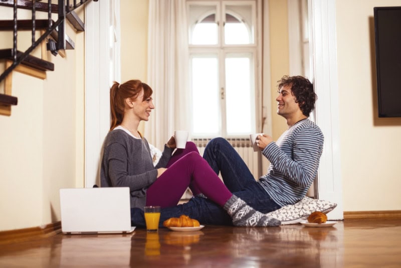 Couple sitting on the floor drinking out of mugs and eating breakfast