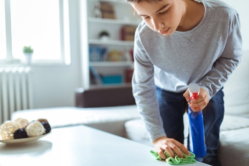 Child cleaning off table to reduce dust in their home.