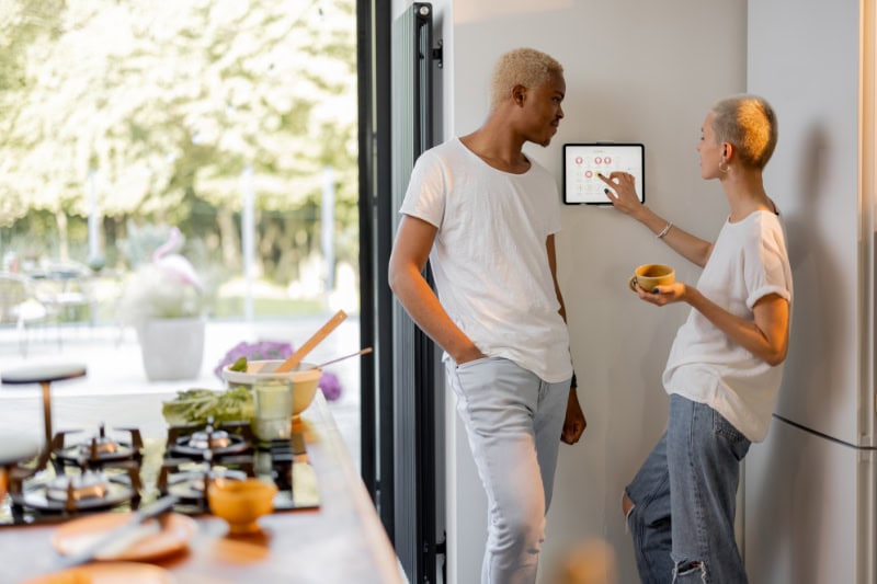 Couple adjusting their home's smart thermostat to represent information about thermostat basics.