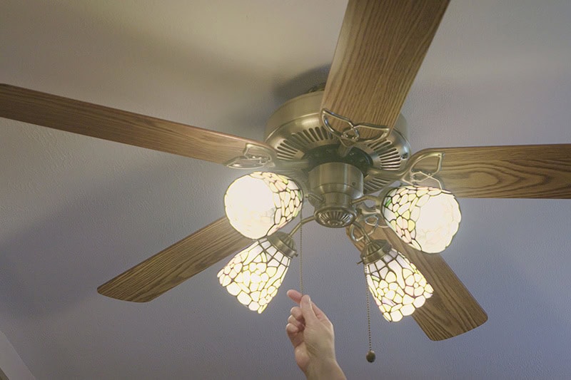 Homeowner turning on ceiling fan to represent energy saving tips information.