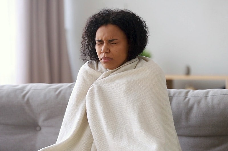 Female homeowner wrapped in a blanket on her couch to represent info about upgrading your furnace.