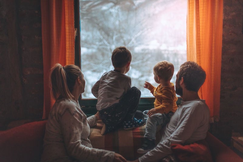 Happy family looking at the snow outside their home to represent winter and your indoor air quality.