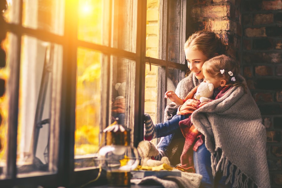 Mom and daughter look out the window while wrapped in a blanket.|Man wrapped in a blanket on the couch holding a warm mug of tea.