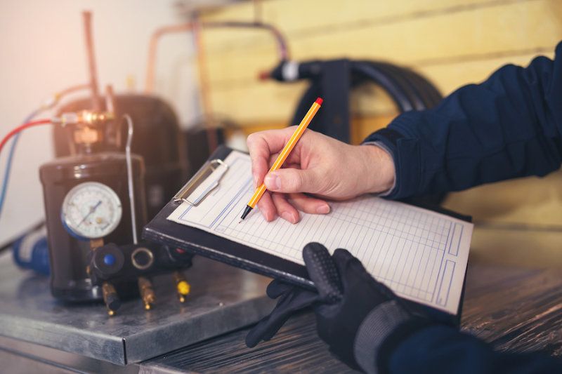 A HVAC Tech uses a clipboard. How Do I Know When I Need a New Furnace?|Male homeowner reading about when you know it's time to buy a new furnace while wife is in kitchen.